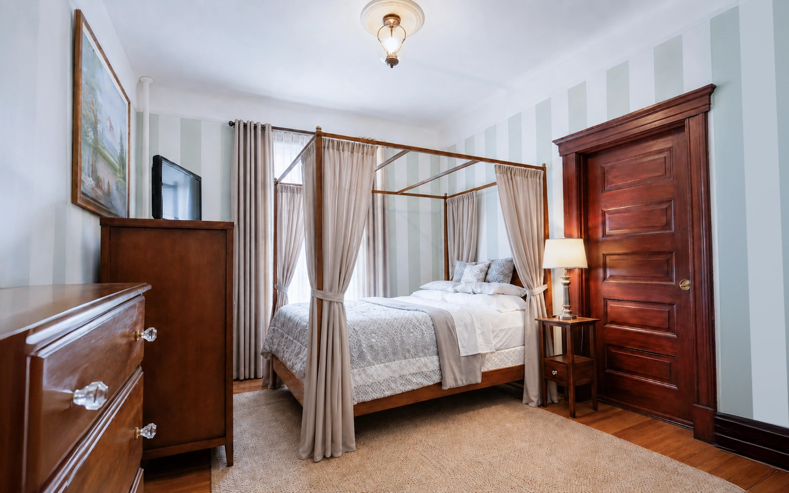 Warm furnished guest room at Idylease with a four-poster bed and tall windows